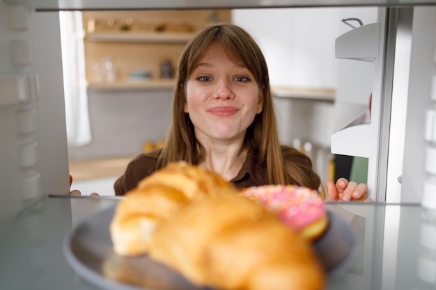 냉장고에 있는 신선한 크루아상과 도넛을 보고 있는 배고픈 소녀