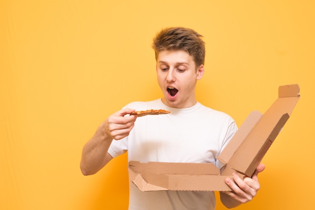 Hungry guy with pizza in his hands is isolated on a yellow