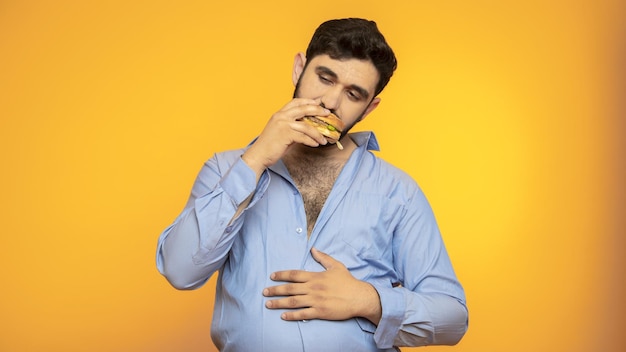 Hungry handsome man holds a hamburger in his hand on yellow background