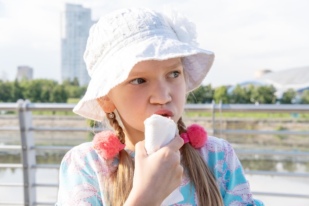 夏のビーチで屋台の食べ物を食べる空腹の子供 フライド ソーセージを食べる帽子の女の子 ファーストフードを食べる幸せな子供