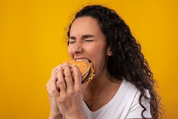 スタジオでハンバーガーを噛むサンドイッチを持っている空腹の女性