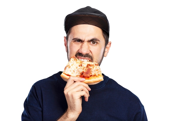 A hungry man in a cap eats a slice of pizza with appetite. Isolated on white background.