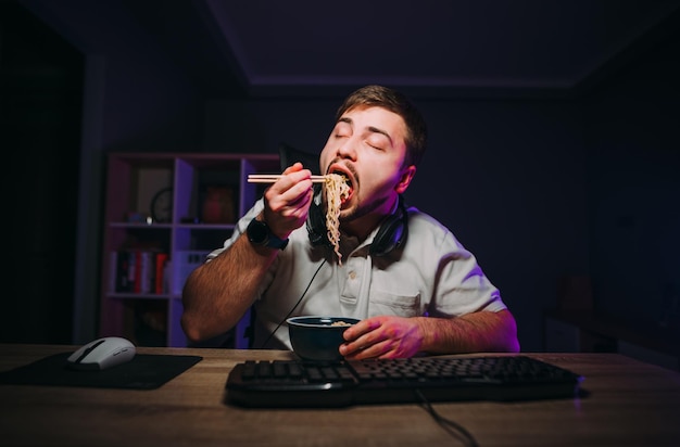 Hungry man eats Asian food with chopsticks at night between work