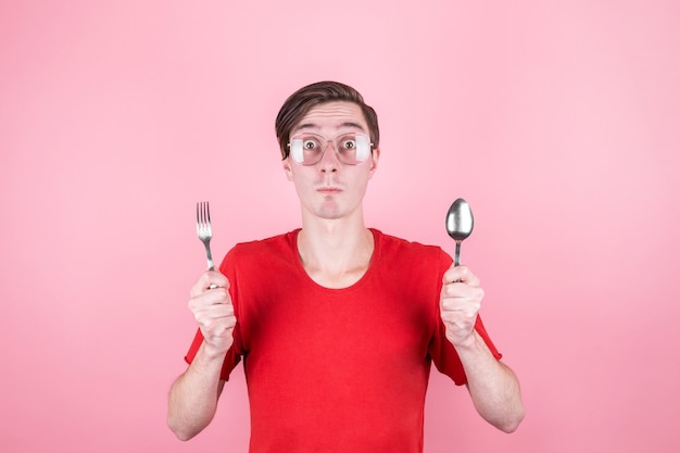 Hungry man holds a fork and spoon in his hands and thinks about delicious food