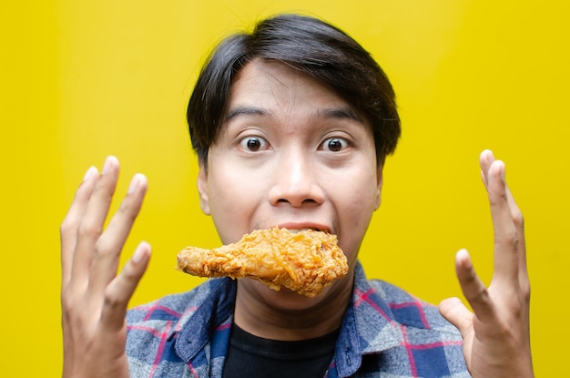 Photo hungry man holds fried drumstick chicken isolated over yellow background