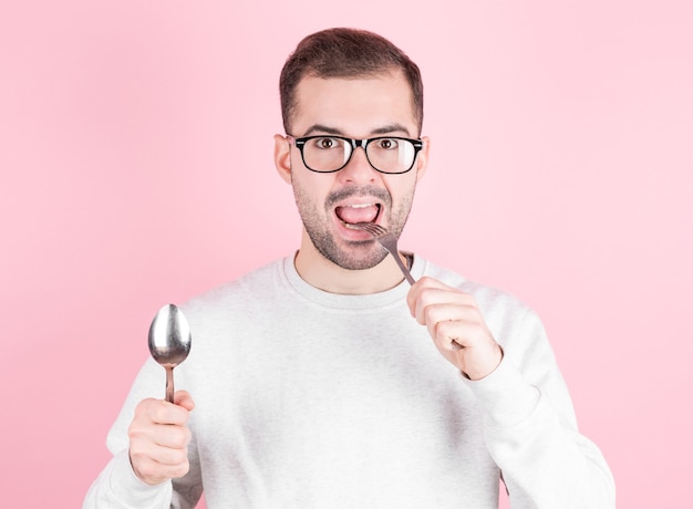 Hungry man licks his lips while holding a fork and spoon in his hands.