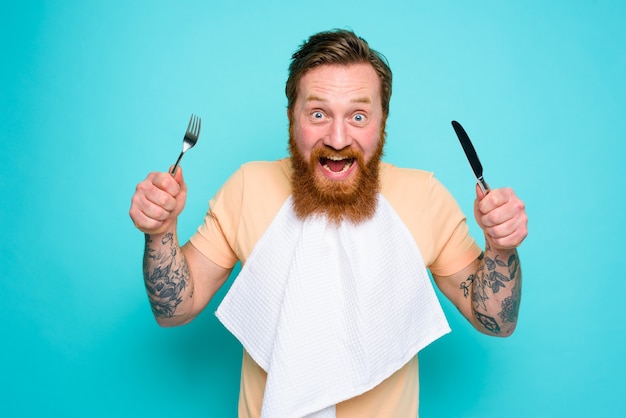 Hungry man with tattoos is ready to eat with cutlery in hand