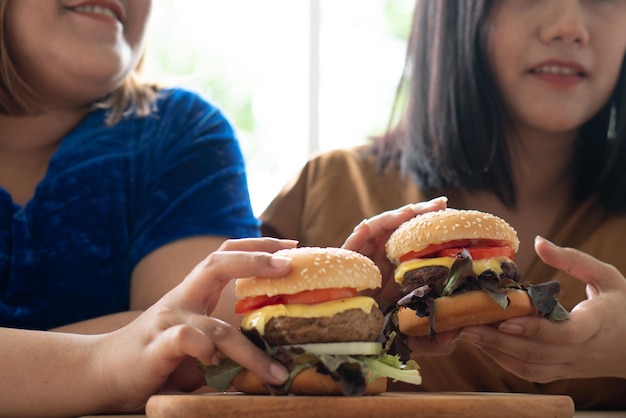 Hungry overweight woman holding hamburger on a wooden plate During work from home gain weight problem Concept of binge eating disorder BED