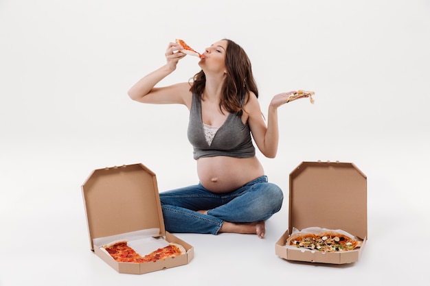 Голодная беременная женщина ест пиццу.