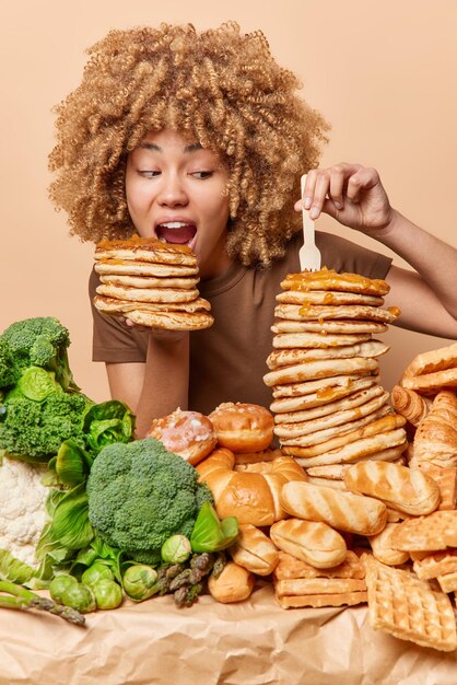 Hungry woman eats delicious sweet pancakes with honey prefers\
eating appetizing food with much calories gives preference to\
unhealthy food over healthy greenery stands near table cheat meal\
concept