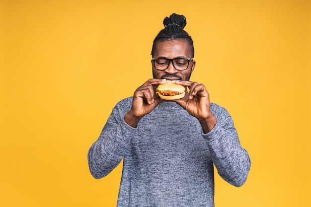 Photo hungry young african american black man eating hamburger isolated over yellow background. diet concept.