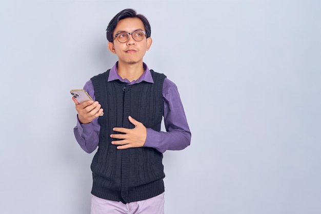 Hungry young Asian man in casual shirt holding smartphone and think of tasty food isolated on white background People lifestyle concept