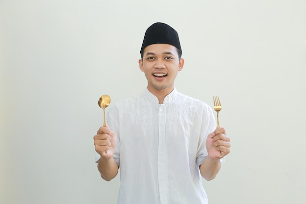 Hungry young Asian Muslim man in Arabic clothes with spoon