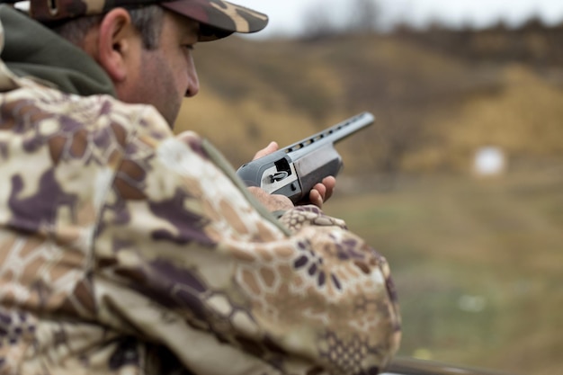 A hunter in camouflage at the shooting range calibrates the\
weapon a man shoots at targets