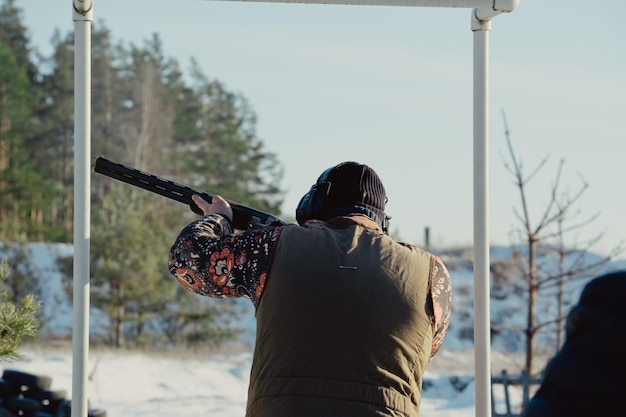 Hunter in camouflage with rifle in winter forest. Hunt concept. Man securing a reserve, on a snowy day. Hunter takes aim from a gun in the snowy forest