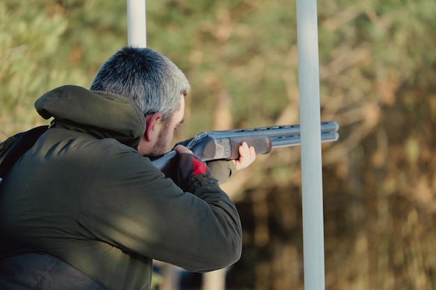 Foto cacciatore in mimetica con fucile nella foresta invernale. concetto di caccia. l'uomo che fissa una riserva, in una giornata nevosa. hunter prende la mira da una pistola nella foresta innevata