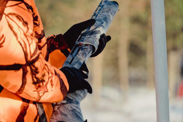 Hunter in camouflage with rifle in winter forest. Hunt concept. Man securing a reserve, on a snowy day. Hunter takes aim from a gun in the snowy forest