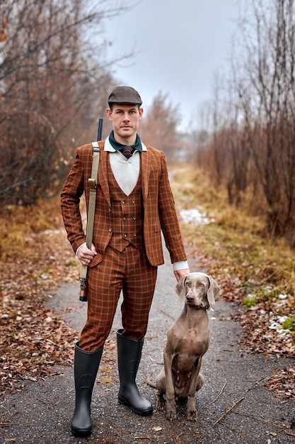 Photo hunter in classic suit with dogs hunting bird woodcock in forest with rifle shotgun brutal male wit