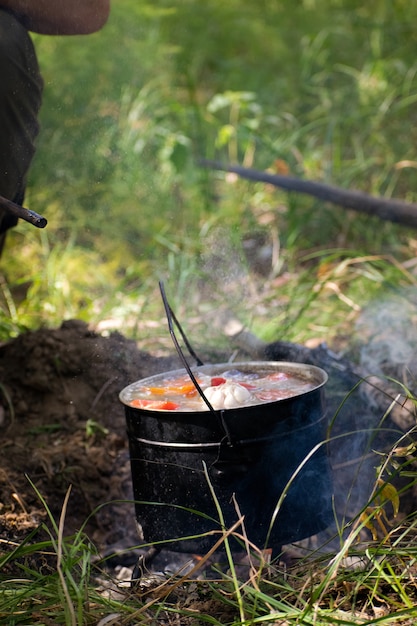 A hunter cooks shurpa in a bowler hat on the fire in nature