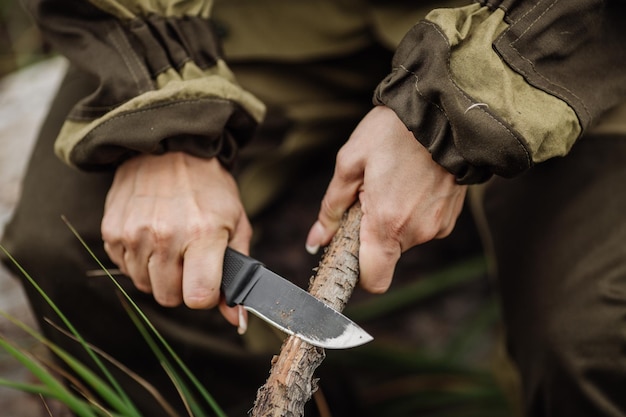 Hunter Girl cuts a stick a knife in the woods