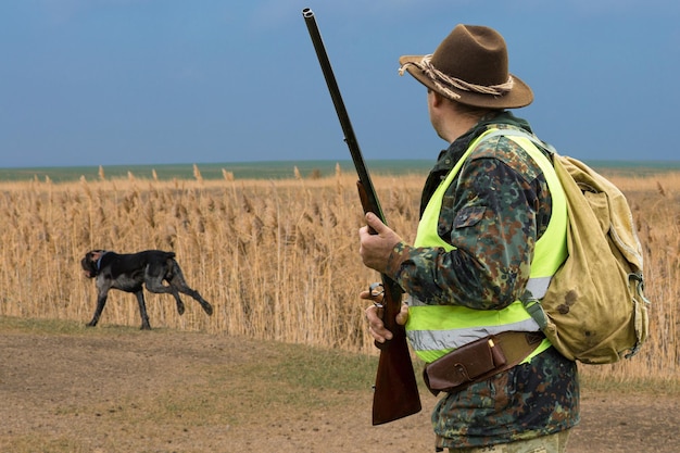 Uomo cacciatore in mimetica con una pistola durante la caccia alla ricerca di uccelli selvatici o selvaggina stagione di caccia autunnale