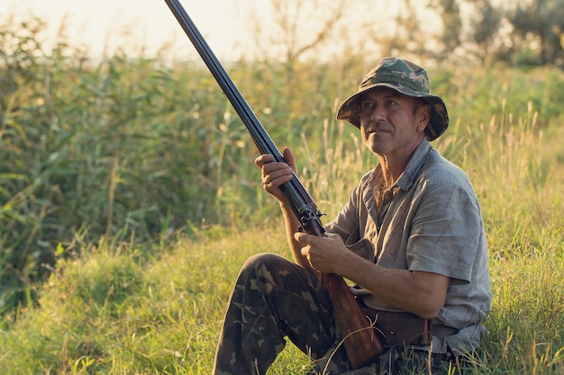 Hunter man in camouflage with a gun during the hunt in search of wild birds or game