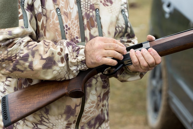 野鳥やゲームを探して狩りをしているときに銃を持ってカモフラージュをしているハンターの男。