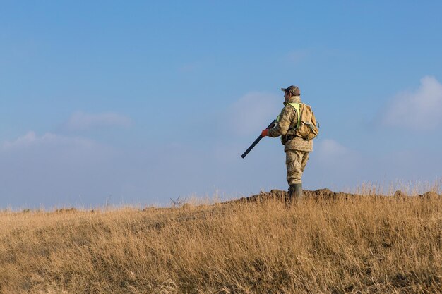 Hunter man in camouflage with a gun during the hunt in search of wild birds or game