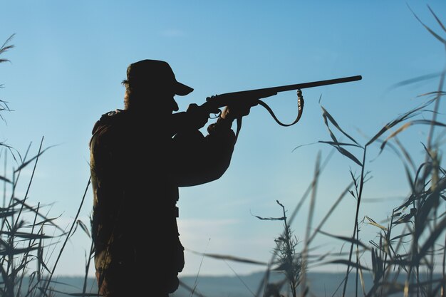 Hunter man in camouflage with a gun during the hunt in search of wild birds