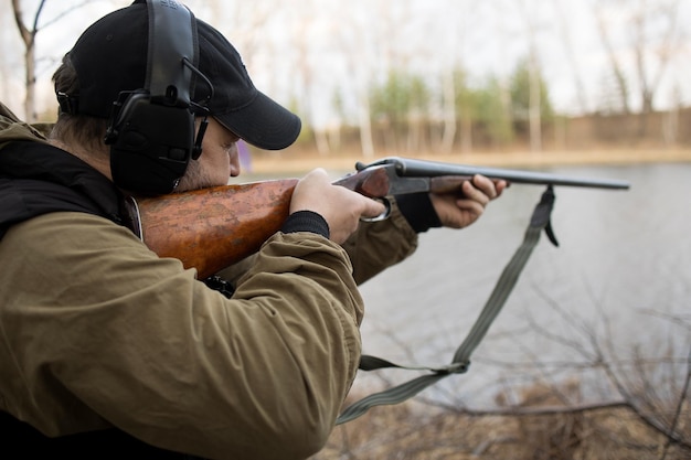 L'uomo cacciatore caccia con una pistola per le anatre sulla riva del fiume