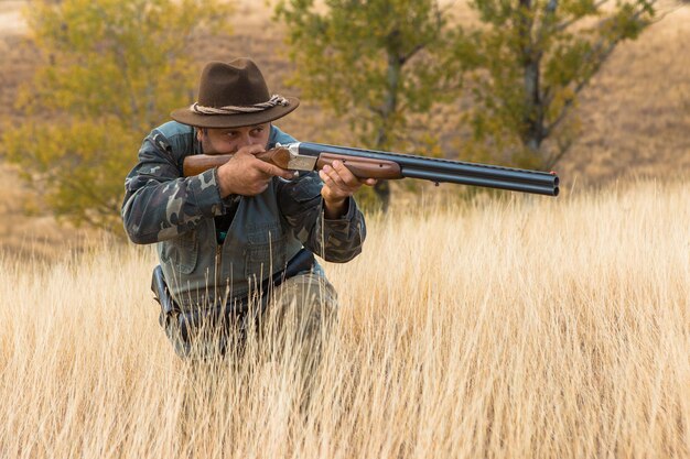 写真 野鳥やゲームの秋の狩猟シーズンを探して狩り中に銃を持ったカモフラージュのハンター男