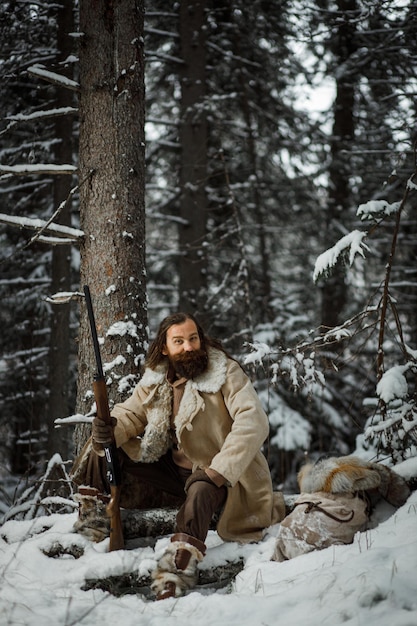 Hunter man in winter warm vintage clothes with gun in winter forest