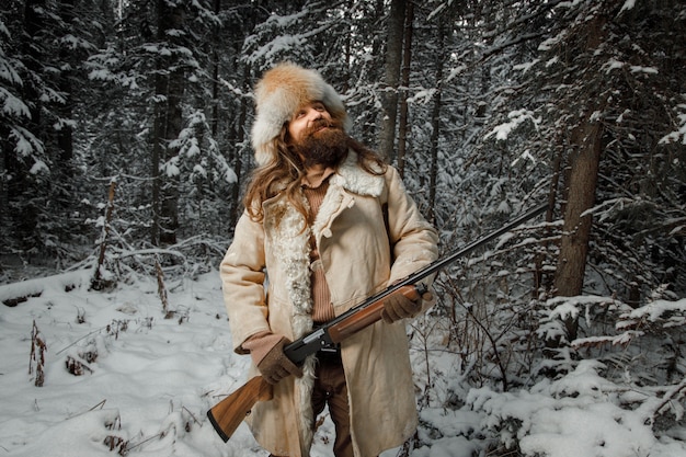 Охотник в винтажной одежде с оружием пробирается через лес