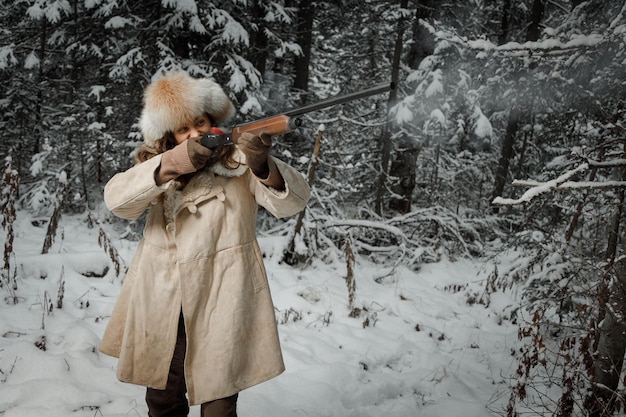 Охотник в винтажной зимней одежде стреляет из ружья в лесу