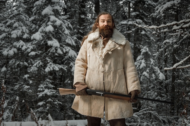 Cacciatore in abiti vintage invernali con la barba nella foresta con la pistola