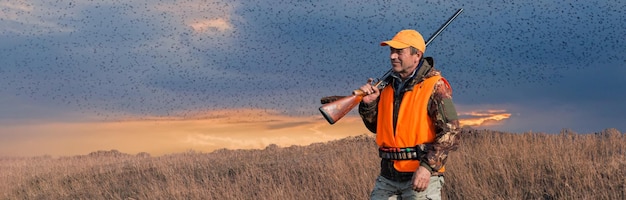 A hunter with a gun in his hands in hunting clothes in the autumn forest in search of a trophy A man stands with weapon