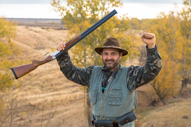 A hunter with a gun in his hands in hunting clothes in the autumn forest in search of a trophy A man stands with weapons and hunting dogs tracking down the game