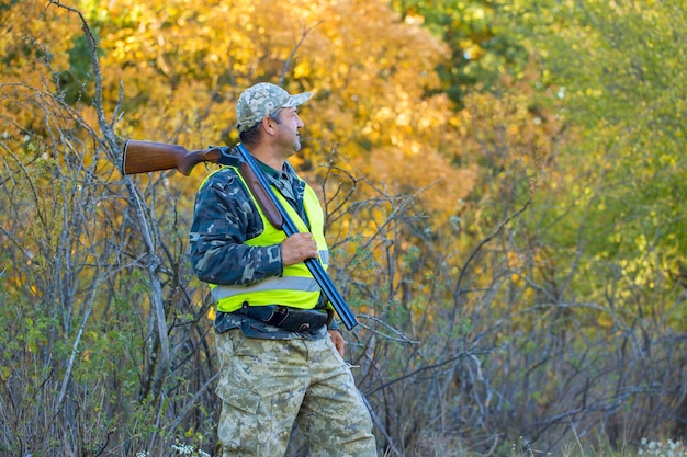a hunter with a gun in his hands in hunting clothes in the autumn forest in search of a trophy a man stands with weapons and hunting dogs tracking down the game