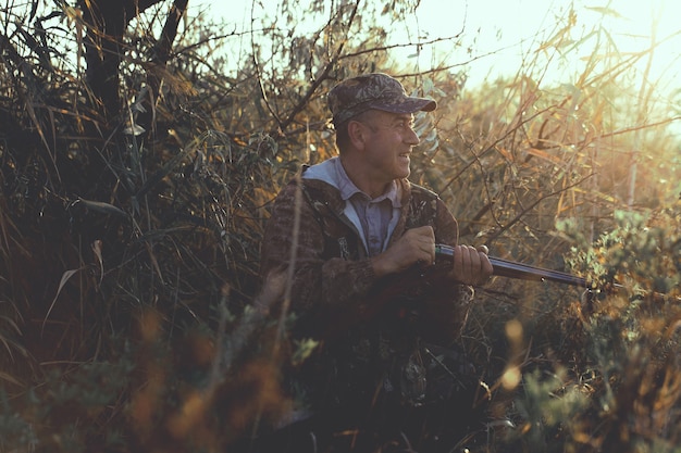 A hunter with a gun in his hands in hunting clothes in the autumn forest in search of a trophy