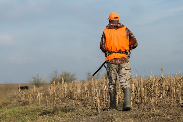 Охотник с ружьем в руках в охотничьей одежде в осеннем лесу в поисках трофея