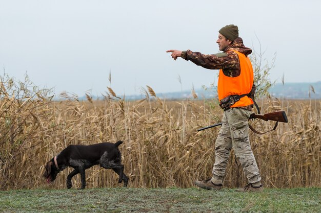 A hunter with a gun in his hands in hunting clothes in the autumn forest in search of a trophy