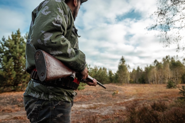 Hunter with a gun in his hands in hunting clothes in the autumn forest 