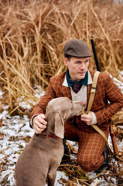 Il cacciatore con la pistola e l'amico di razza del cane weimaraner in natura si siedono insieme nella natura della campagna incredibile