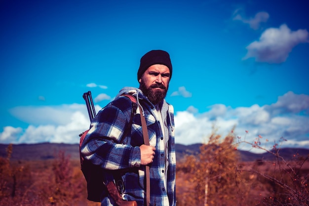 Hunter with shotgun gun on hunt Bearded hunter man holding gun and walking in forest Autumn