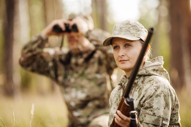 Hunter with shotgun looking through binoculars in forest