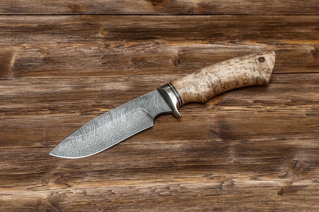 Hunting damascus steel knife handmade on a wooden surface, close-up