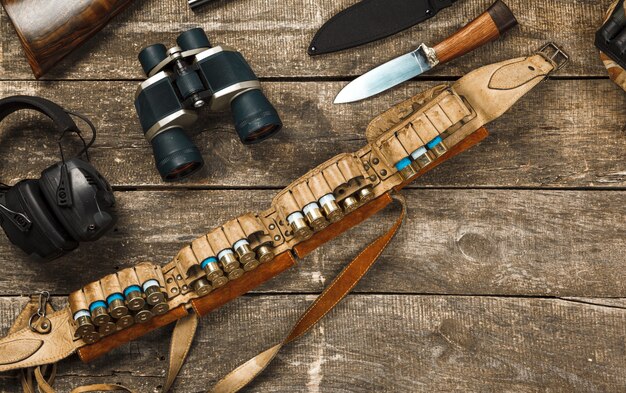 Hunting equipment on old wooden background including rifle knife binoculars and cartridges