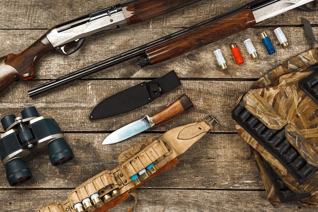 Hunting equipment on old wooden background including rifle knife binoculars and cartridges