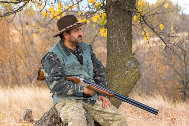 Hunting period autumn season open A hunter with a gun in his hands in hunting clothes in the autumn forest in search of a trophy A man stands with weapons and hunting dogs tracking down the game