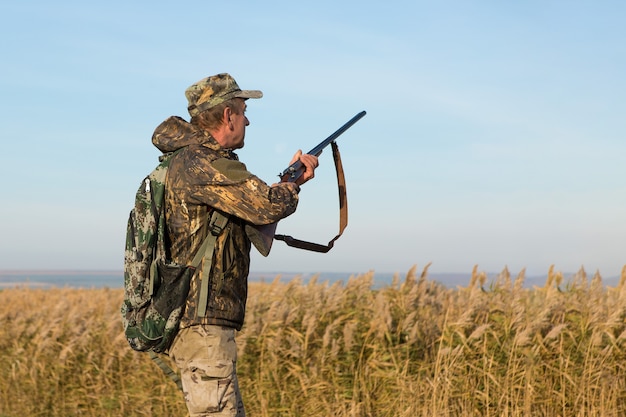 Hunting period, autumn season open. A hunter with a gun in his hands in hunting clothes in the autumn forest in search of a trophy. A man stands with weapons and hunting dogs tracking down the game.